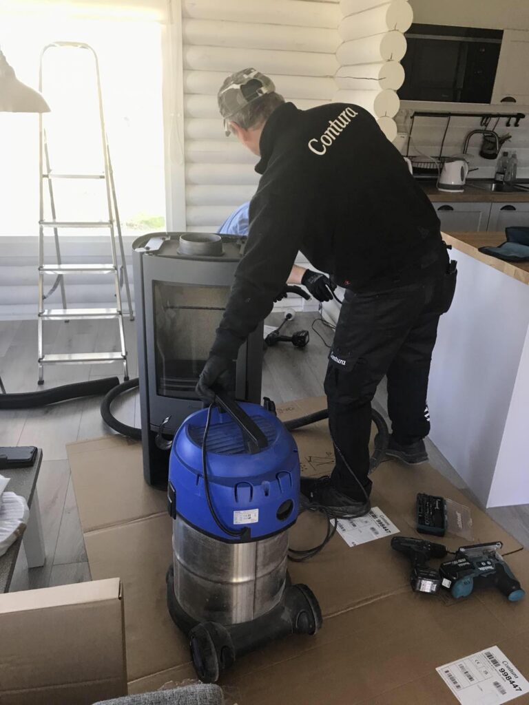 bild på byggarna som jobbar i stugan förfullt med att såga och dammsuga för att installera kaminen